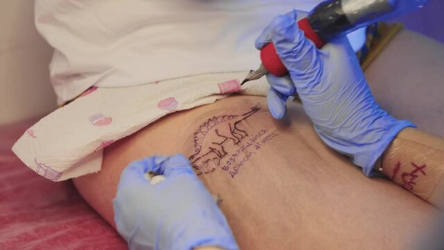 Tattoo master drawing an outlines of dinosaur tattoo on the leg