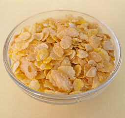 Bowl of cereal corn flakes on a yellow background. High key style