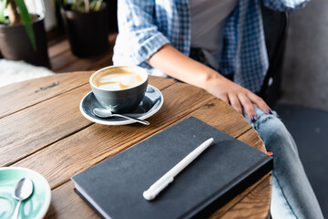 cropped of woman sitting at table with cup of coffee and notebook in cafe