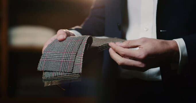 Cinematic shot of young businessman is choosing fabrics for his new custom tailored suit by designer in a luxury tailoring atelier. Concept of fashion, handmade, hand craft, couturier and business.