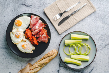 Top angle view on sunny side up eggs prosciutto coppa Capocollo dry meat and homemade ajvar paprika salad on the table as dinner or breakfast meal