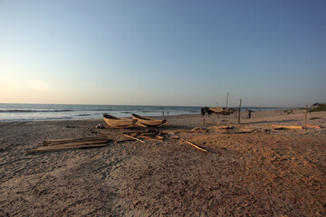 wide angle horizontal photography of a pink and blue sunset over Atlantic ocean shore, with sandy beach, wooden boats and a fishermans shelter, outdoors in the Gambia, Africa