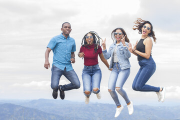 group of four latin american young women and man outdoors smiling happy and jumping high looking to camera in a summer day vacation trip with nature in background