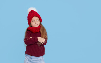 Winter portrait of happy child girl wearing knitted red hat, snood and sweater. Wow face. Blue background. childrens winter entertainment