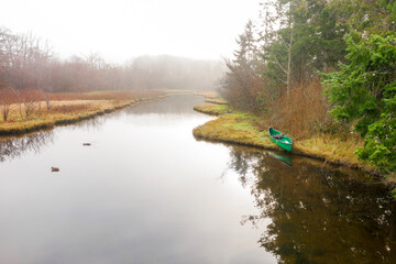 Green Canoe on a Slough. Aerial shot of a beautiful watershed draped in fog with a green canoe pulled up on shore. Seen on Lummi Island, Washington.