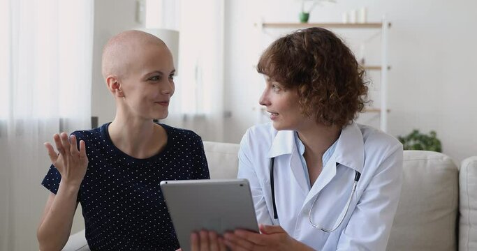 Focused 40s professional oncologist holding digital tablet, explaining treatment strategy to interested young woman with cancer disease, asking about health condition, showing chemo test results.