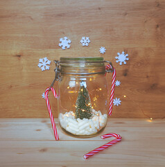 View of a jar filled with white capsules and a Christmas tree with lights and Christmas ornaments on wooden background with copy space. Medical or pharmacology background.