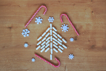 Christmas tree made of white capsules surrounded with red and white Christmas decorations and ornaments on wooden background with copy space. Medical, medication or pharmacy background.