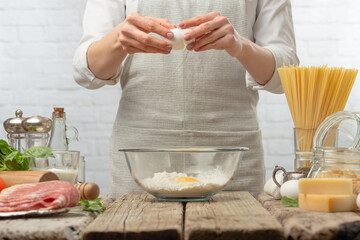 The professional chef breaks egg into glass bowl for cooking pasta alla carbonara. Backstage of preparing traditional italian dish on white background. Frozen motion. Cookbook illustration.