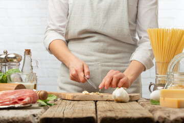 Professional chef cuts with knife garlic on wooden board for cooking pasta alla carbonara. Backstage of preparing traditional italian dish on white background. Frozen motion. Cookbook illustration.