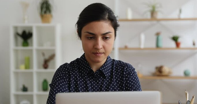 Serious Indian student woman sit indoor use laptop working hard, thinking over task, problem issue solution, learn new app, prepare for university exams, during fruitful workday, study process concept