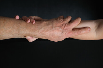 Fototapeta premium male and female hands together on black background, old skin with wrinkles and veins, concept of health, age-related changes, love, tender relationship of a couple in life