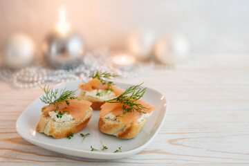 Festive canapes from baguette bread with smoked salmon, cream cheese and dill garnish on a plate,...