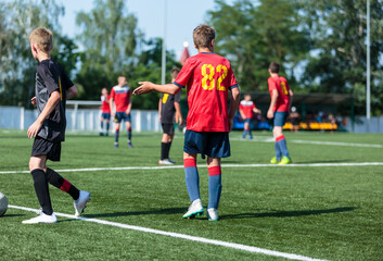 Fototapeta premium Boys in red sportswear plays football on field, dribbles ball. Young soccer players with ball on green grass. Training, football, active lifestyle for kids 
