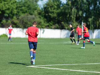 Boys in red sportswear plays football on field, dribbles ball. Young soccer players with ball on green grass. Training, football, active lifestyle for kids	