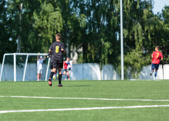 Boys in red sportswear plays football on field, dribbles ball. Young soccer players with ball on green grass. Training, football, active lifestyle for kids	
