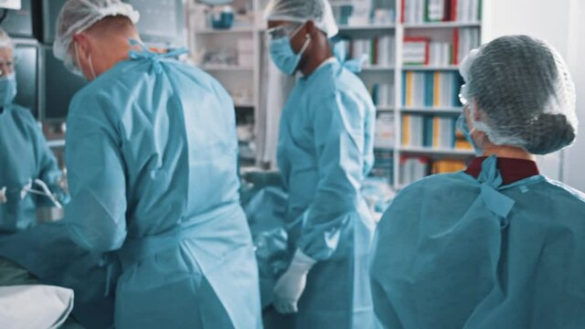 Back view of the young female caucasian assistant or intern wearing medical face mask and protective cap going at her workplace while with preparing for the operation with doctors at the medical ward