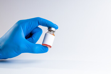 medical person holding medicine vial with red liquid and blank label over gray background. copy space. vaccine concept