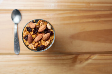 Fototapeta na wymiar Cup of granola and yogurt with raisins, almonds and peanuts on wooden table showing the concept of tasty, healthy food. Top view with copy space.