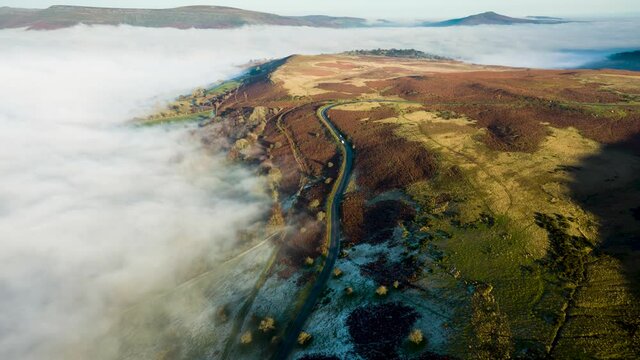 Aerial hyperlapse of low clouds and fog moving next to a narrow, winding mountain road