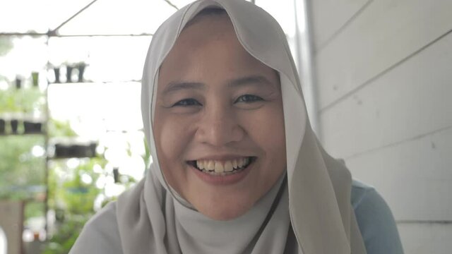 Portrait of beautiful Asian muslim woman smiling at camera, woman stiting relaxing outside her home