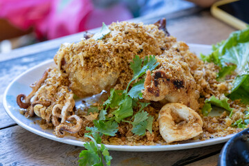Fried squid with galic and coriander on top in white dish on wood table, ready to eat.