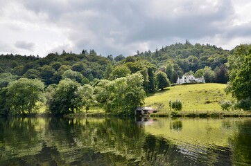 Fototapeta na wymiar Beautiful house on a green hill among tees with a lake view.