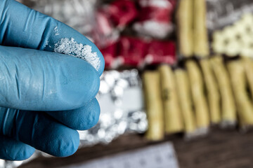 evidence of smuggling traffic: drug powder in the hand of a forensic expert against the background of other arrested materials, cocaine, heroin, spice
