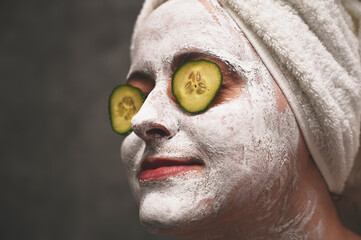 A woman applies a face mask and uses cucumber slices to solve skin problems around the eyes. An...