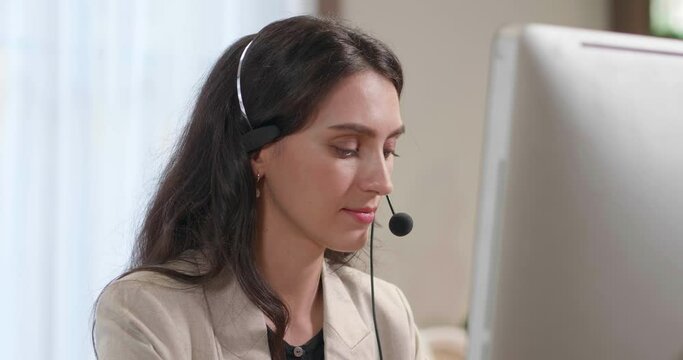 Businesswoman wearing headset working in office with computer screen to support remote customer or colleague. Female call center, telemarketing, customer service on telephone video conference call