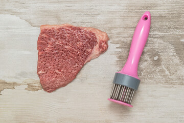 A big steak of beef and a device for pounding meat on a wooden background.
