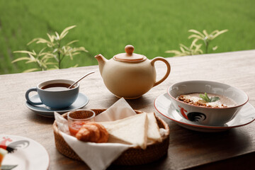 Breakfast with pot of tea, smoothie bowl, fruits and croissant served on the tale with view on rice terrace