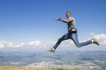 one black skinned latin american young man outdoors and jumping high looking to camera in a summer...