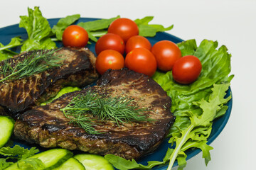 Beef steaks on a plate with cucumber, tomato and herbs.