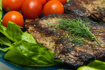 Beef steaks on a plate with cucumber, tomato and herbs.
