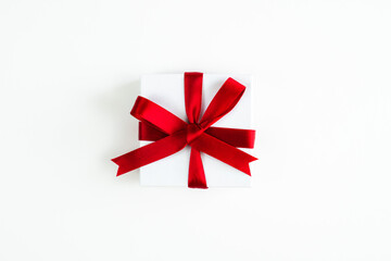 Beautiful holiday or Christmas background image of a small red ribbon wrapped white box present centered on a white backdrop with copy space surrounding the gift.