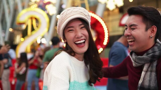Merry Christmas and Happy New Year! Young  asian couple with Christmas lights looks at phone in fair. Happy couple celebrating Christmas  outdoor together.