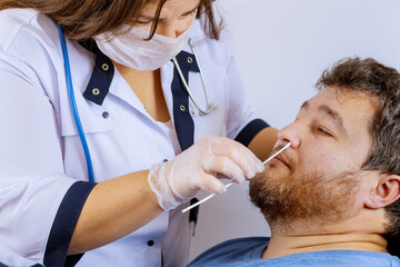 Fototapeta premium Female medical worker taking a swab for coronavirus sample plr test from potentially infected man with surgical face masks personnel taking nasal sample