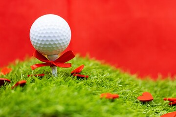 Golf Wedding or Valentine's Day with golf ball red ribbon is tee off on green grass on red background