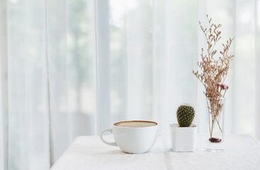 Close up white coffee cup with small cactus in white pot and dry leaf in glass on table in living room