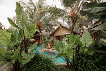 Girl relaxing and eating floating breakfast in jungle pool surrounded with palm trees on luxury...
