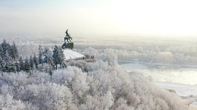 Monument to Salavat Yulaev on a mountain among snow-covered trees with a river in the background. A beautiful view of the winter embankment opens. Drone shot. High quality 4k footage.