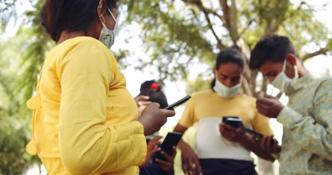 Slow-motion static shot portrait of group of friends wearing identical surgical face mask busy on their individual mobile phone as they ignore each other, digital addiction anti-social detox 