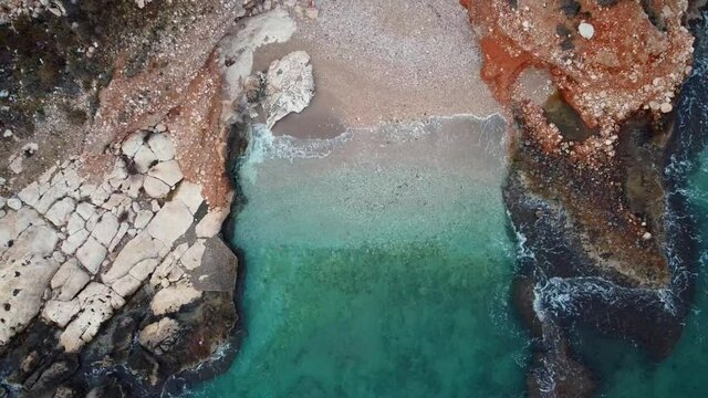 Small backwater on rocky sea coast. Evening surf. Top down zoom out aerial view. Ascending drone aerial footage