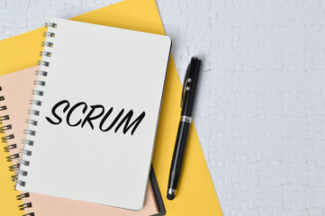 Top view of pen, yellow paper and notebooks written with text SCRUM. Business concept.