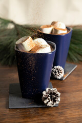 Elegant mugs with hot chocolate and marshmallows with cinnamon sprinkled on top - hot chocolate served on the christmas table