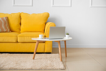 Stylish sofa and laptop near light wall in room