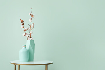 Vases with cotton flowers on stylish table near color wall in room