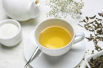 Cup of aromatic green tea and dry leaves on wooden background