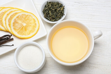 Cup of hot tea, bowl with dry leaves and lemon on wooden background